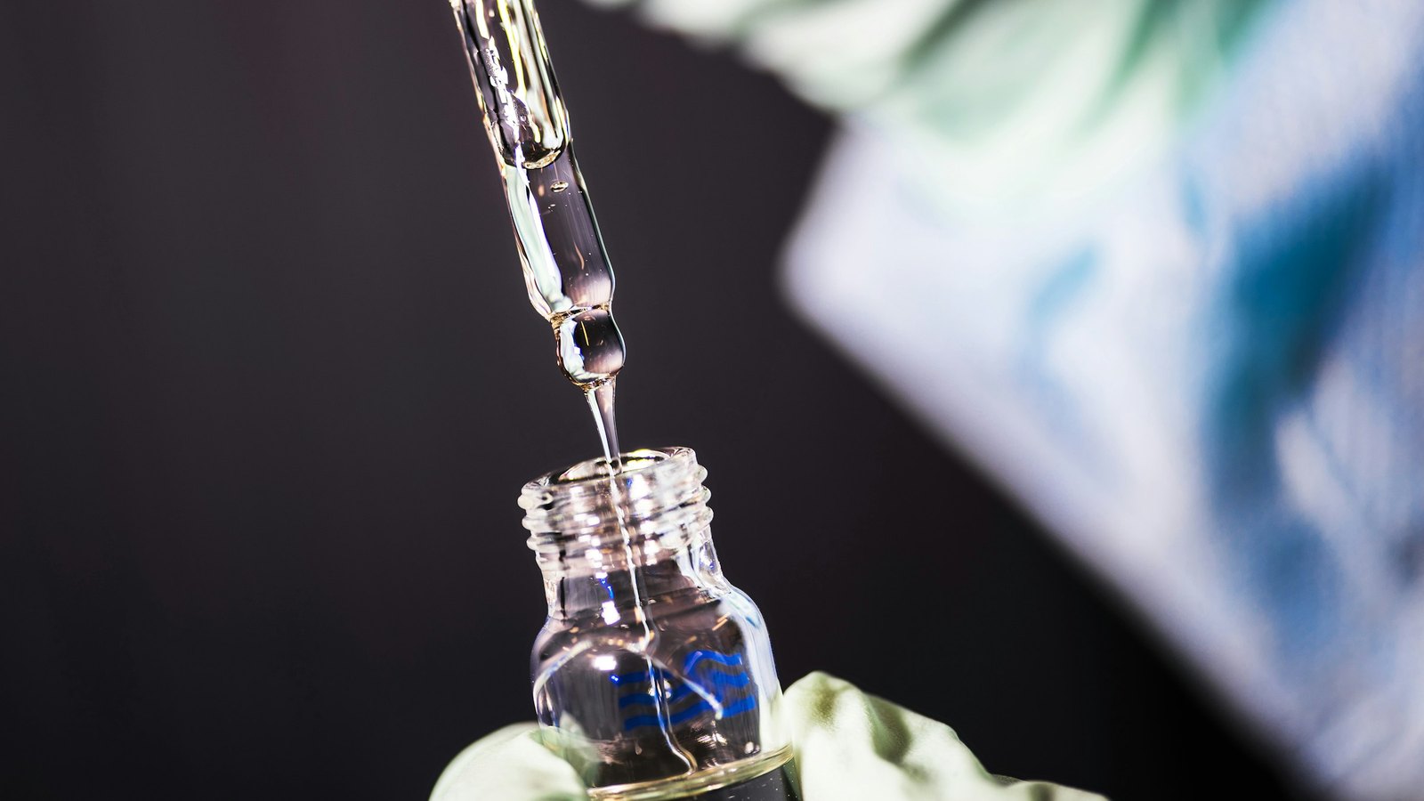 Liquid dropping from a pipette into a small glass vial