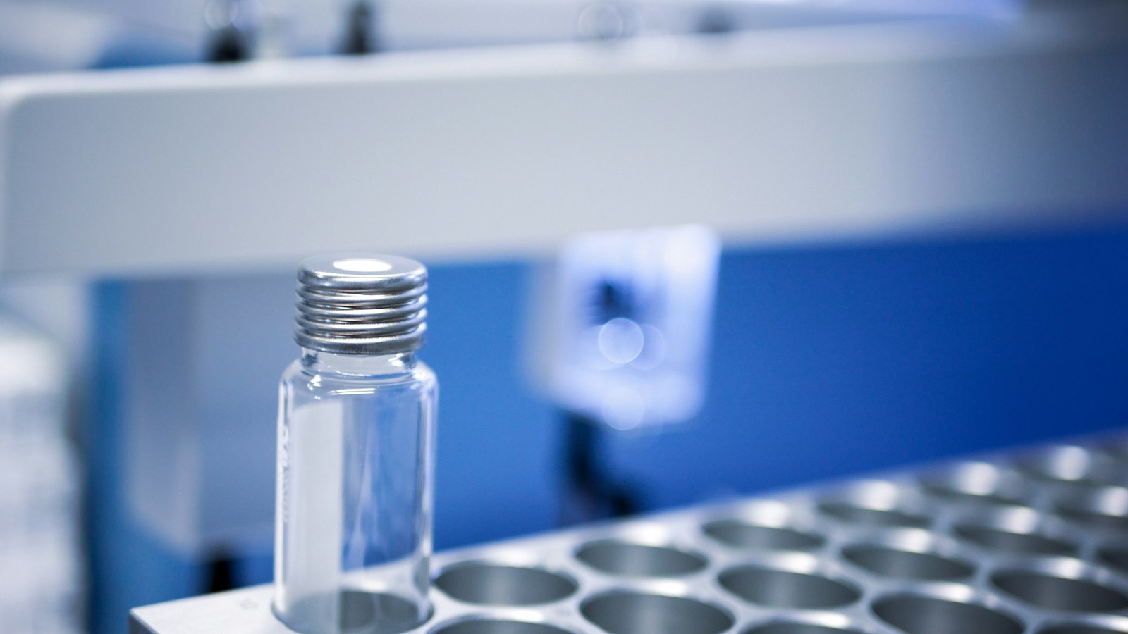 Glass vial with a metal screw cap in a sample rack, blue background